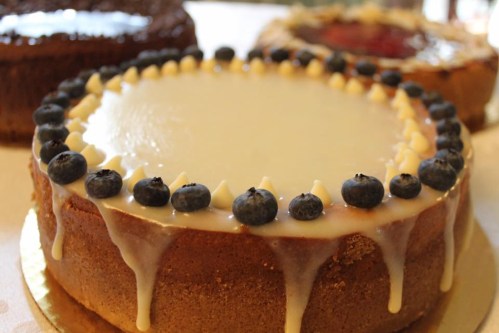 A round cake topped with a smooth white glaze and blueberries, with decorative icing around the edge.