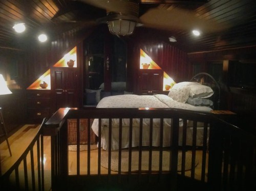 Cozy bedroom with wooden walls, a large bed, and warm lighting, featuring decorative lamps and a circular rug.