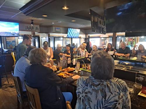 A lively bar scene with patrons enjoying food and drinks, gathered around a long counter and watching a TV.