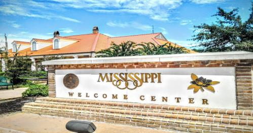 Sign for the Mississippi Welcome Center, featuring a brick structure and a bright blue sky in the background.