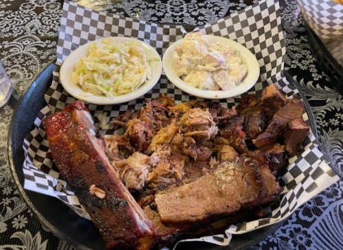 A platter of assorted barbecue meats, including ribs and pulled pork, served with coleslaw and potato salad.