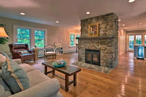 Cozy living room with a stone fireplace, wooden floors, and large windows letting in natural light.