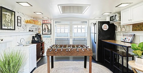A bright, modern kitchen with a foosball table, black appliances, and vintage decor on the walls.