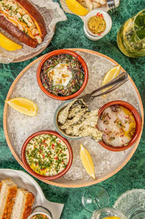 A platter of seafood dishes on ice, featuring dips, garnishes, and lemon wedges, set on a green table.