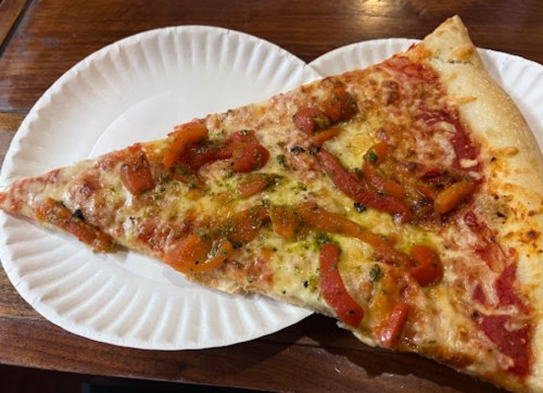 A slice of pizza topped with melted cheese, red peppers, and herbs on a paper plate.