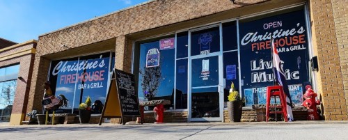 Exterior of Christine's Firehouse Bar & Grill, featuring large windows, a sign for live music, and colorful decorations.