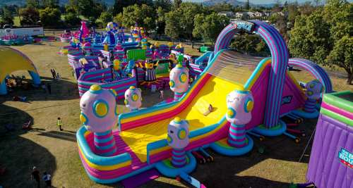 A colorful inflatable water slide at a fun park, surrounded by various inflatable attractions and people enjoying the day.