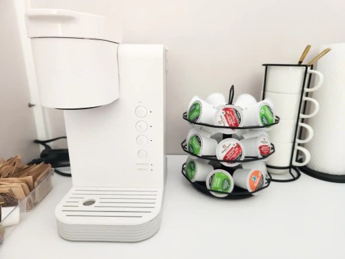 A white coffee maker next to a rotating holder filled with colorful coffee pods.