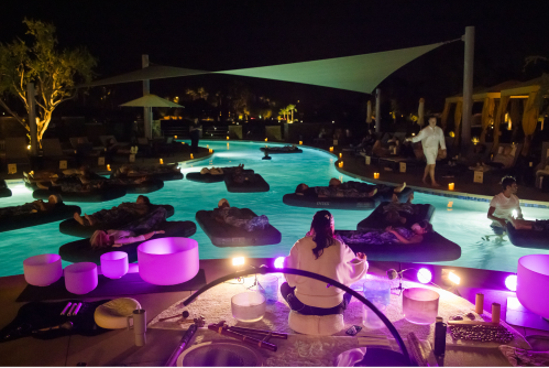 A serene nighttime scene at a poolside spa, with guests relaxing on floating mats surrounded by soft lighting.