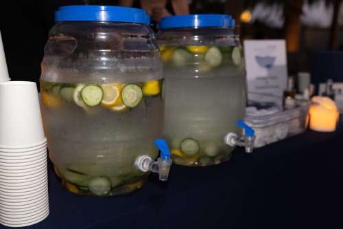 Two large beverage dispensers filled with infused water, featuring slices of lemon and cucumber, on a table with cups.