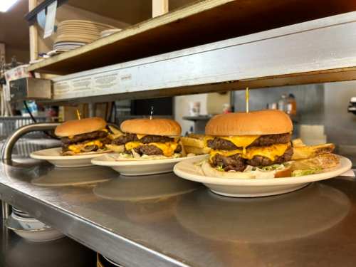Three cheeseburgers with fries on plates, sitting on a counter in a diner.