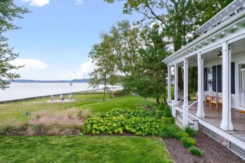 A serene lakeside view featuring a porch, lush greenery, and a calm water scene under a clear blue sky.