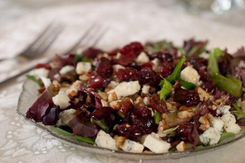 A colorful salad with mixed greens, cranberries, pecans, and blue cheese on a decorative plate.