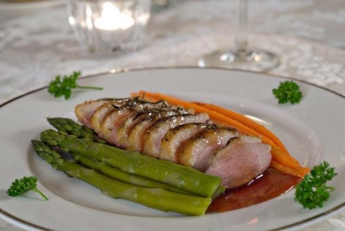 A plated dish featuring sliced meat, asparagus, and carrot puree, garnished with parsley on a fine dining table.