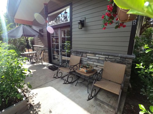 A cozy outdoor seating area with two chairs and a small table, surrounded by greenery and flowers.