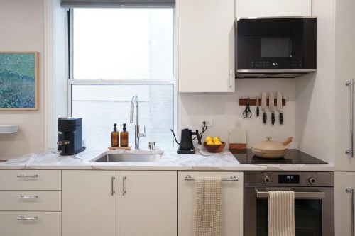 Modern kitchen with a sink, coffee maker, and cooking utensils, featuring a minimalist design and natural light.
