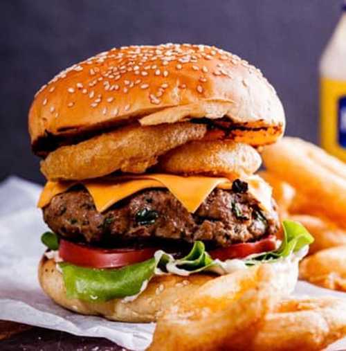 A juicy cheeseburger with lettuce, tomato, and onion rings, served with crispy fries on the side.