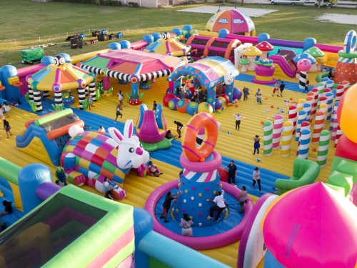 A colorful inflatable playground with various structures, children playing, and vibrant decorations in a grassy area.