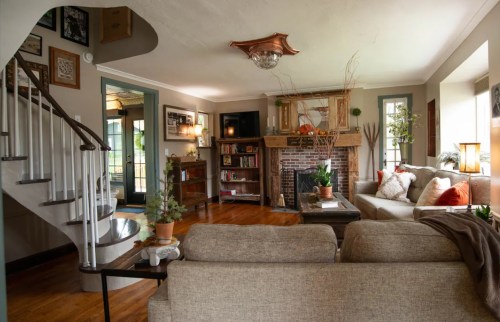 Cozy living room with a fireplace, comfortable seating, and decorative plants, featuring a staircase in the background.