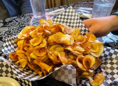 A large basket of crispy, golden potato chips served on a checkered paper.