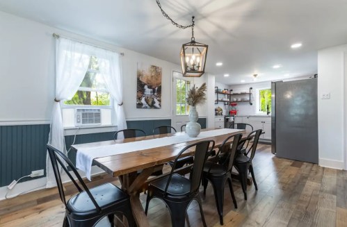 A bright dining area with a wooden table, black chairs, and a modern kitchen in the background.