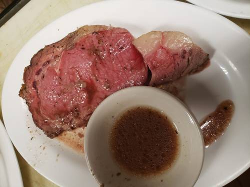 A slice of medium-rare roast beef on a plate, accompanied by a small bowl of brown sauce.