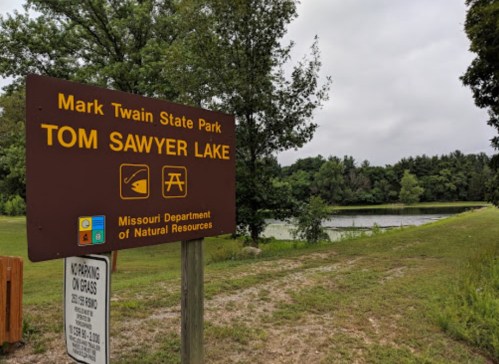 Sign for Tom Sawyer Lake at Mark Twain State Park, surrounded by trees and a calm water view.