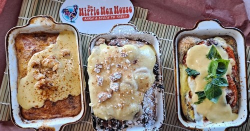Three baked dishes in white serving trays, topped with creamy sauces and garnishes, on a bamboo mat.