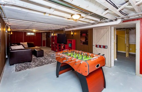 A cozy basement game room featuring a foosball table, couch, TV, and warm lighting.