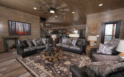 Cozy living room with dark wood walls, plush sofas, a rustic coffee table, and warm lighting.