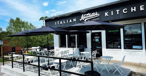 Outdoor seating area with white tables and chairs under black umbrellas at Nicoletto's Italian Kitchen.