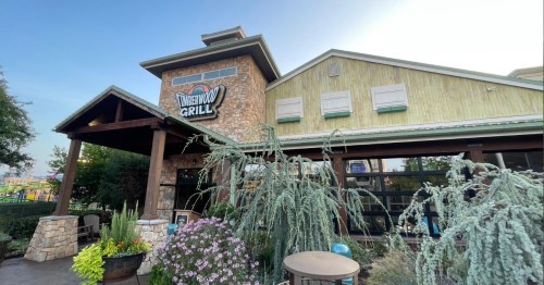 Exterior of Sweetwood Grill, featuring a stone facade, wooden accents, and surrounding greenery and flowers.