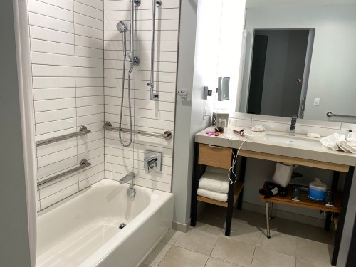 A modern bathroom featuring a bathtub, shower, sink, and a mirror, with neutral tile and minimal decor.
