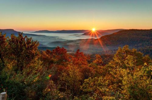 A stunning sunrise over misty valleys, surrounded by colorful autumn foliage and distant mountains.
