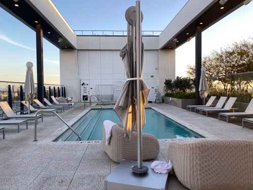 Rooftop pool area with lounge chairs, a small pool, and umbrellas under a clear sky.