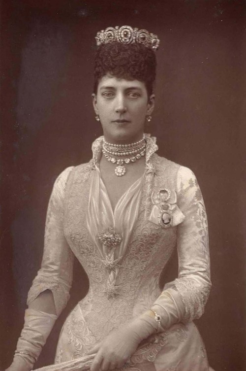 A formal portrait of a woman in an ornate gown, adorned with jewelry and a tiara, exuding elegance and sophistication.