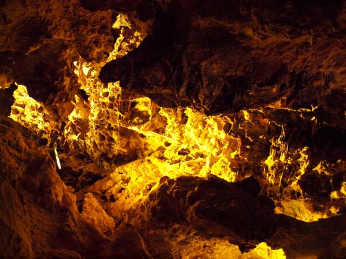 Glowing orange and yellow rock formations illuminated in a dark cave, creating a dramatic, textured landscape.