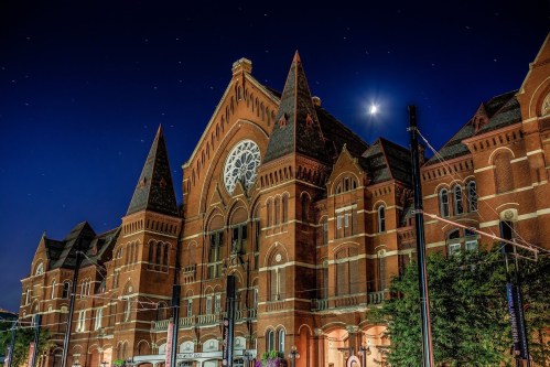Historic building with pointed towers and a large rose window, illuminated under a night sky with stars and a crescent moon.