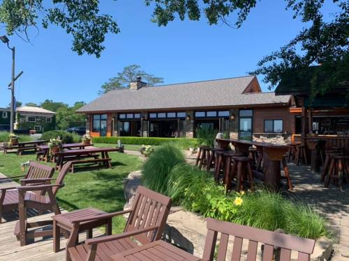 A sunny outdoor view of a rustic restaurant with wooden seating and lush greenery.