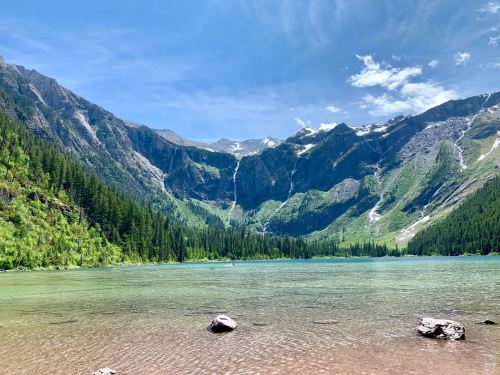 A serene lake surrounded by lush green mountains and a clear blue sky, with a waterfall cascading in the background.