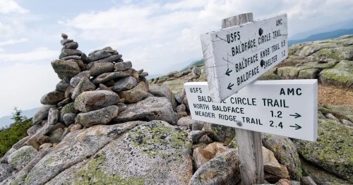 Signpost at a rocky mountain summit, indicating trails to Baldface Circle, North Baldface, and Meader Ridge.