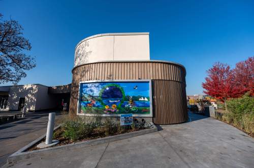A modern building with a colorful mural, surrounded by trees and a clear blue sky.