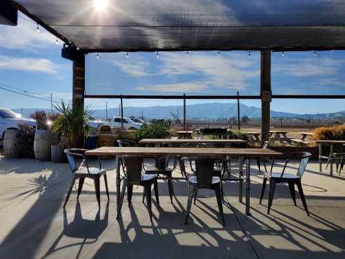 Outdoor dining area with a long table and chairs, overlooking mountains and a clear blue sky.