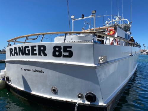 A white boat named "Ranger 85" docked in a marina with clear blue skies and water.