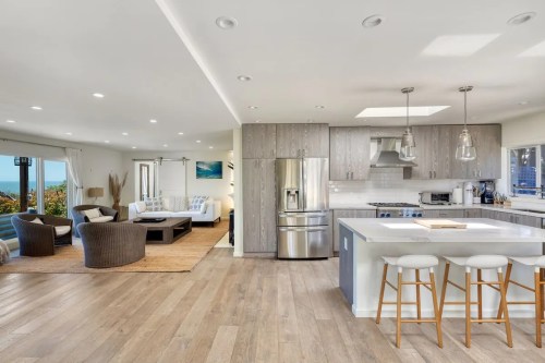 Modern open-concept living space with a kitchen, dining area, and cozy seating, featuring large windows and natural light.