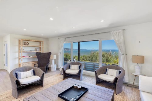 Bright living room with coastal views, featuring wicker chairs, a wooden coffee table, and large sliding glass doors.