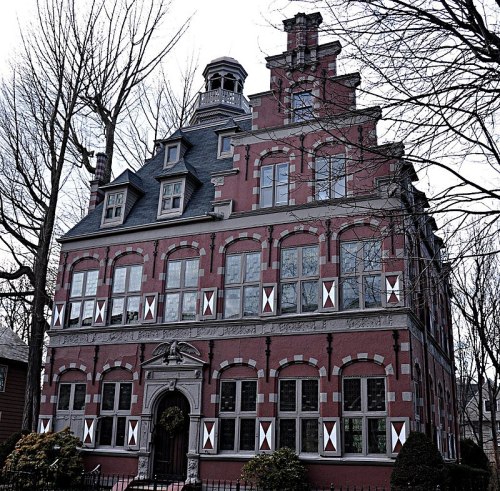 A large, ornate brick building with multiple windows and a distinctive roof, surrounded by bare trees.