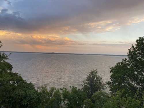 A serene view of a lake at sunset, with colorful clouds and trees framing the scene.