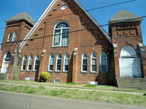 Historic brick church with arched windows and a tall steeple, set against a clear blue sky.