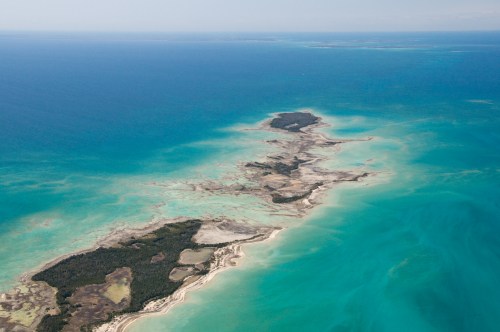 Aerial view of a tropical island surrounded by turquoise waters and sandy shores, with lush greenery visible.
